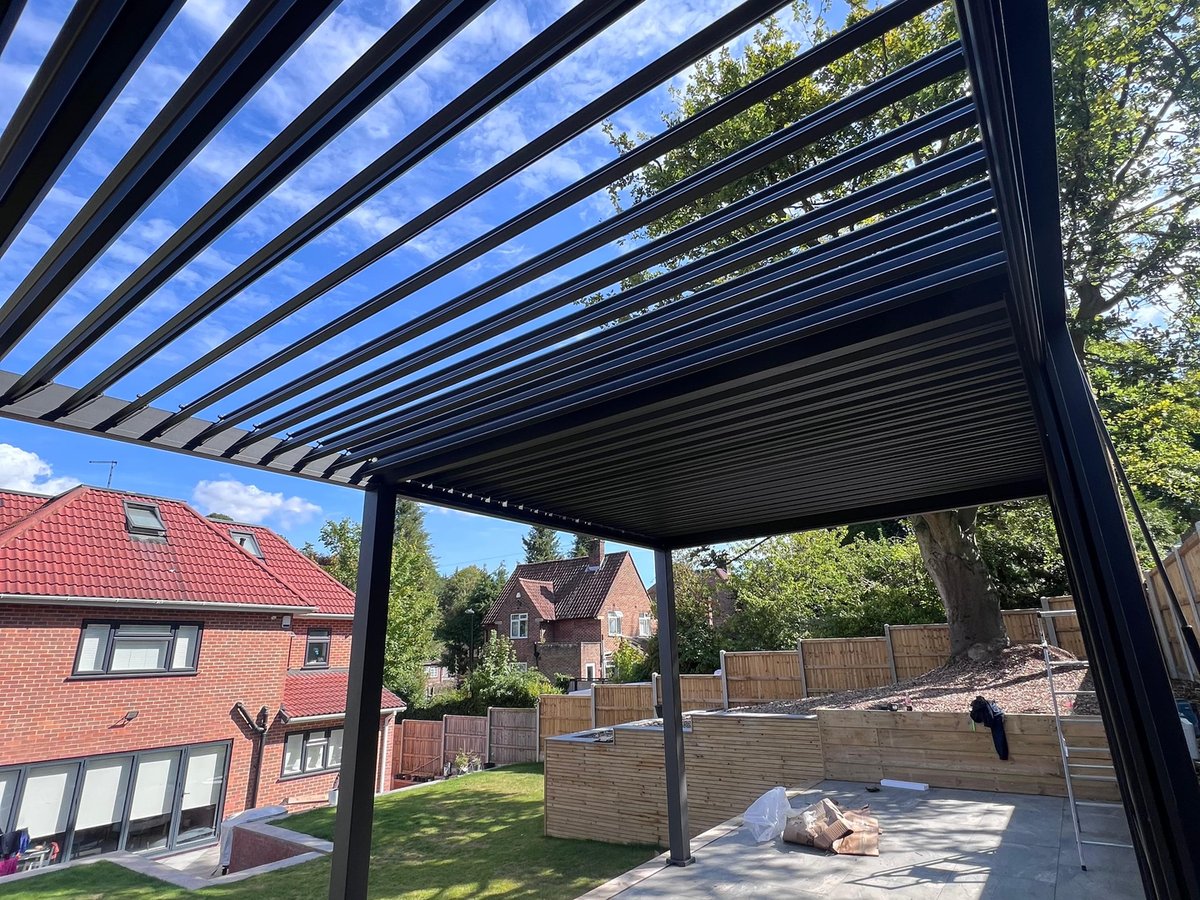 6 metre by 3 metre anthracite aluminium louvred pergola over a porcelain patio, shot from below against a blue sky