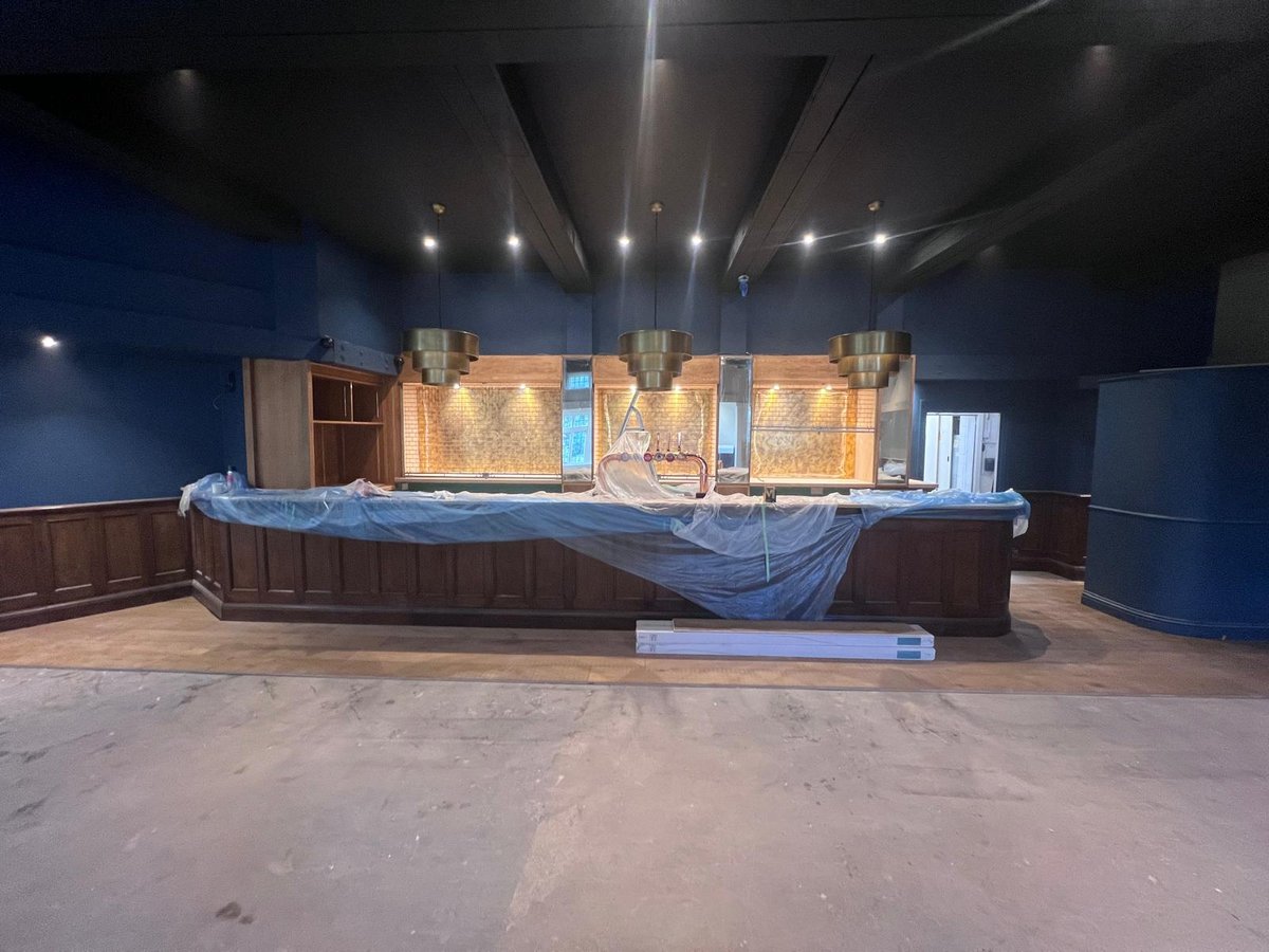 Refurbished panelled oak bar with subway-tiled back-bar, three brass pendant lights and deep navy walls at Thatcher's, Effingham