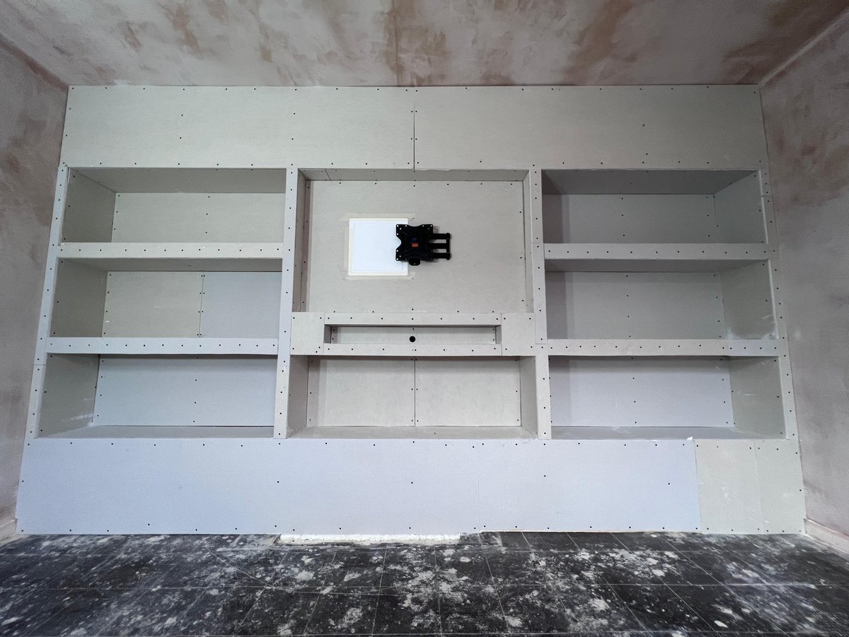 Bespoke full-width media wall boarded in plasterboard with recessed TV bay, open display shelves either side and under-cabinetry