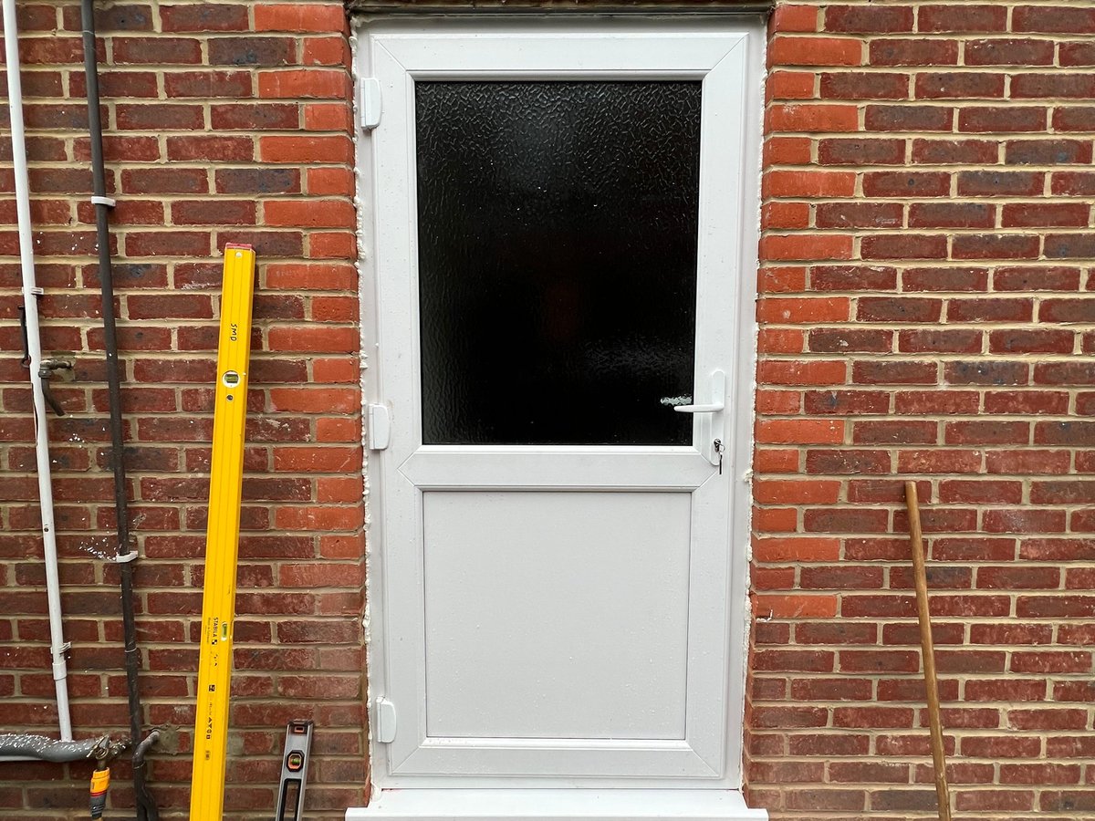 New white UPVC back door installed into a red-brick wall where a high-level PVC window used to be, in Redhill